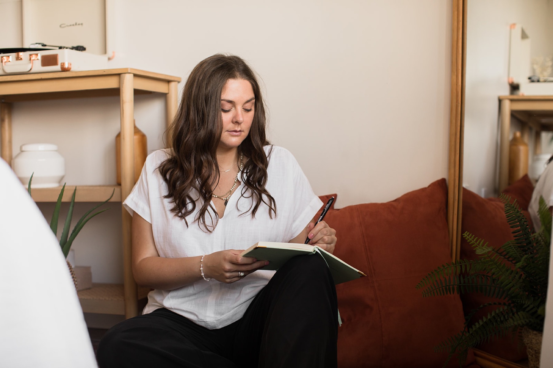 Heather Flynn journaling on a couch in a warm, plant-filled studio